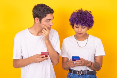 Arka planda izole edilmiş cep telefonlarına bakan genç çift