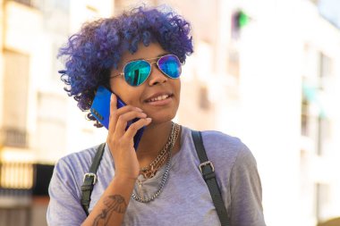 Şehirde güneş gözlüklü şehir kızı cep telefonuyla konuşuyor.