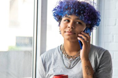 Penceresinde cep telefonu ve kahve olan Afro-Amerikalı genç bir kadın.