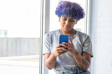 Penceresinde akıllı telefonu olan genç bir kadın.