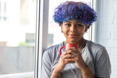 Penceresinde bir fincan kahve olan genç bir kadın.