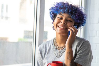 Penceresinde cep telefonu ve kahve olan genç bir kadın.