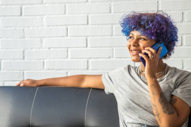 Kadın cep telefonuyla evdeki kanepede oturuyor.