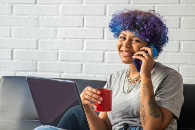 Bilgisayarı, cep telefonu ve fincanı olan genç bir kadın.