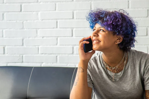 Güzel Afro-Amerikalı kadın cep telefonuyla kanepede oturuyor.