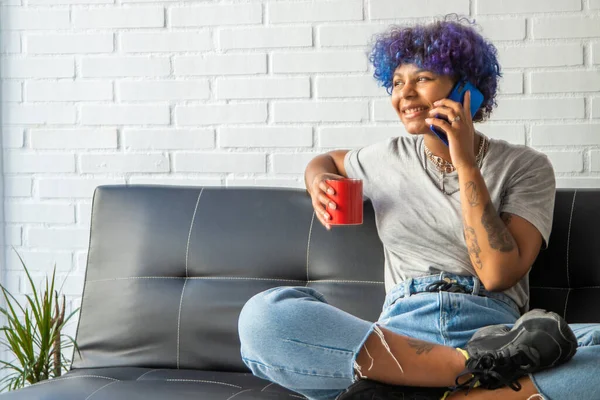 woman on the sofa at home with cup of coffee talking on mobile phone