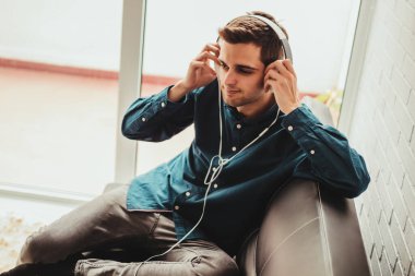 Apartmandaki kanepede oturan genç adam cep telefonu ve kulaklıklarıyla.
