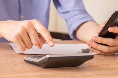 Ön planda hesap makinesi ve cep telefonu olan eller