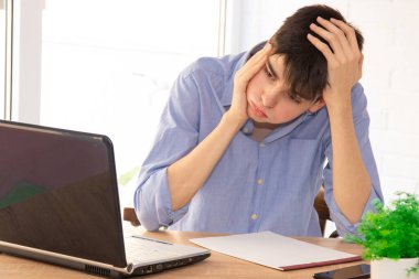 Masasında bilgisayar olan ve yorgunluk ya da yorgunluk belirtileri gösteren bir öğrenci.