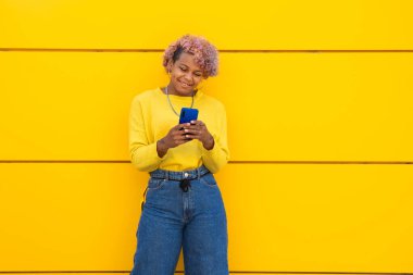 Sarı şehir duvarında cep telefonu olan mutlu kız.