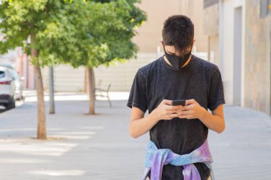 Sokaktaki maskeli ve cep telefonlu genç adam.