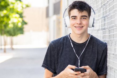 Sokaklarda cep telefonu ve kulaklığı olan genç bir çocuk.