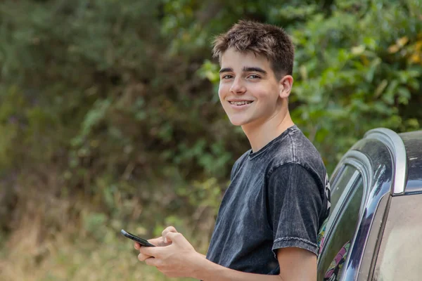 Dışarıda cep telefonu ve arabası olan genç bir çocuk.
