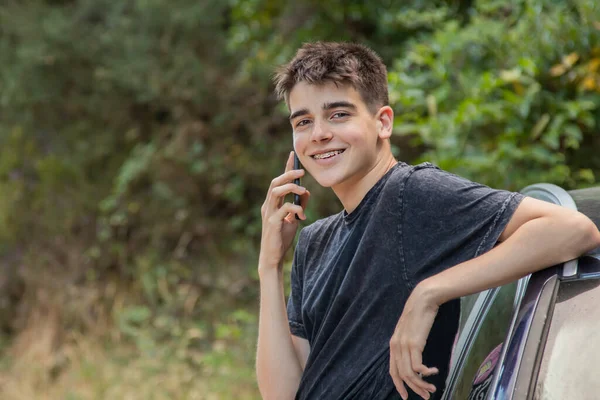 Dışarıda cep telefonu ve arabası olan genç bir çocuk.