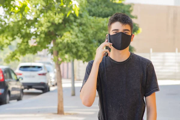 Sokaktaki maskeli ve cep telefonlu genç adam.