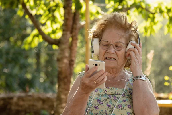 在户外带手机和耳机的老年妇女 — 图库照片