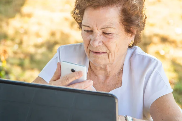 在户外带手机和电脑的老年妇女 — 图库照片