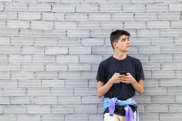 屋外の街の壁に携帯電話を持った10代の少年 — ストック写真