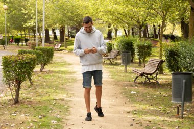 Dışarıda yürüyen sakallı ve cep telefonlu çekici bir genç.