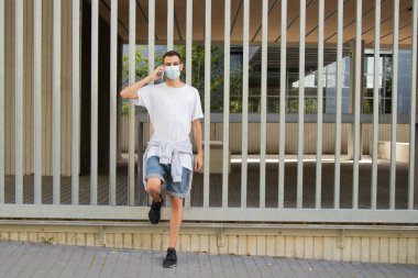 Maskeli ve cep telefonlu genç bir adam.