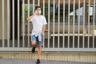 Maskeli ve cep telefonlu genç bir adam.