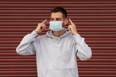 Sokakta maskeli genç bir adam ve arka planı kırmızı kör.