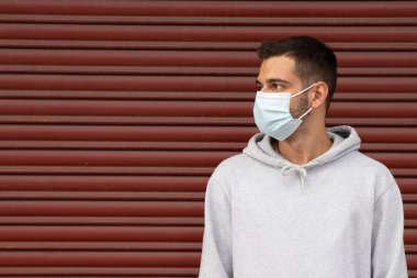 Sokakta maskeli genç bir adam ve arka planı kırmızı kör.