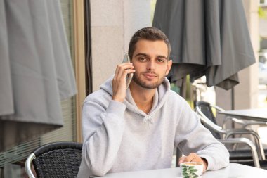 Terasta cep telefonlu genç bir adam kahve içiyor.