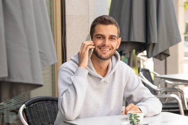 Terasta cep telefonlu genç bir adam kahve içiyor.