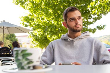 Kafe terasında cep telefonlu genç bir adam.