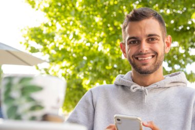 Kafe terasında cep telefonlu genç bir adam.