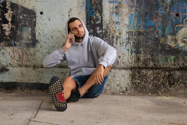 若い男が携帯電話を持って通りの床に座り — ストック写真