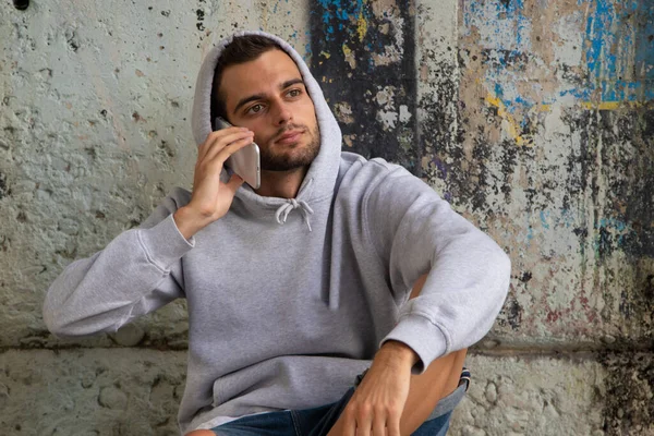 young man sitting on the street floor with mobile phone, stains or paint chips on the wall without intellectual property