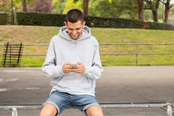 Glimlachende Jongen Typen Kijken Naar Mobiele Telefoon Zitten Straat — Stockfoto