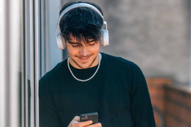 Kulaklık ve cep telefonu olan genç bir adam ya da öğrenci.