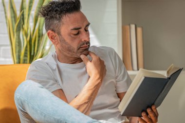 Evdeki genç adam kanepede oturmuş kitap okuyor.