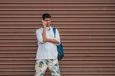 Sokak duvarında sırt çantası ve cep telefonu olan şehir genci