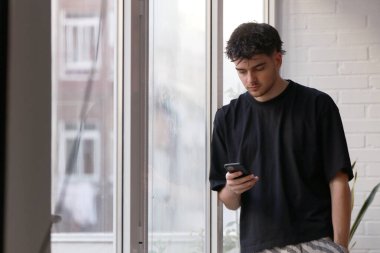 Genç bir erkek cep telefonuna bakıyor.