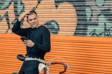 Şehir arka planında cep telefonu ve bisikleti olan şık bir genç adam.