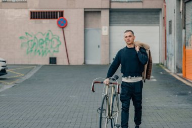 Bisikletli genç adam sokakta yürüyor.