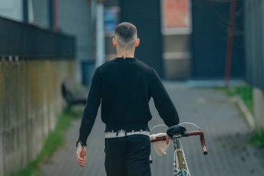 Bisikletli genç adam sokakta yürüyor.