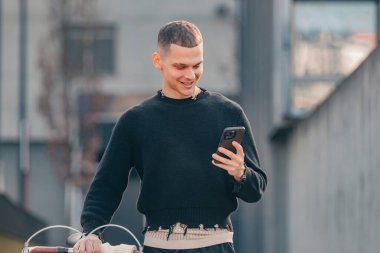 Sokakta yürüyen cep telefonu ve bisikleti olan genç adam.