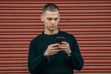 Sokakta kırmızı arka planda cep telefonu ve bisikleti olan genç adam.