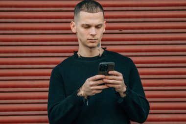 Sokakta kırmızı arka planda cep telefonu ve bisikleti olan genç adam.