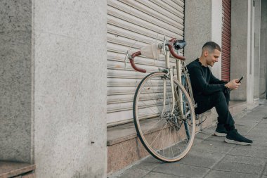 Genç adam cep telefonuyla sokakta oturuyor.