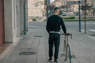 Sırtında bisikletle sokakta yürüyen genç adam.