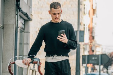 Genç adam sokakta telefon ve bisikletle yürüyor.