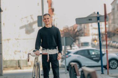 Genç adam bisikletle sokakta yürüyor.