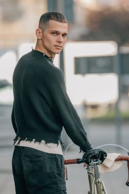 Sırtında bisikletle sokakta yürüyen genç adam.