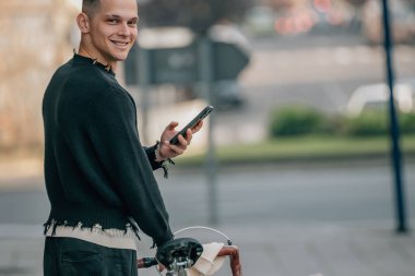 Bisiklet ve cep telefonuyla sokakta yürüyen genç adam.